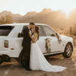 Bride and groom beside a white Rolls-Royce Cullinan in the Arizona desert at sunset