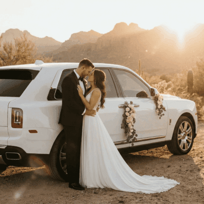 Bride and groom beside a white Rolls-Royce Cullinan in the Arizona desert at sunset
